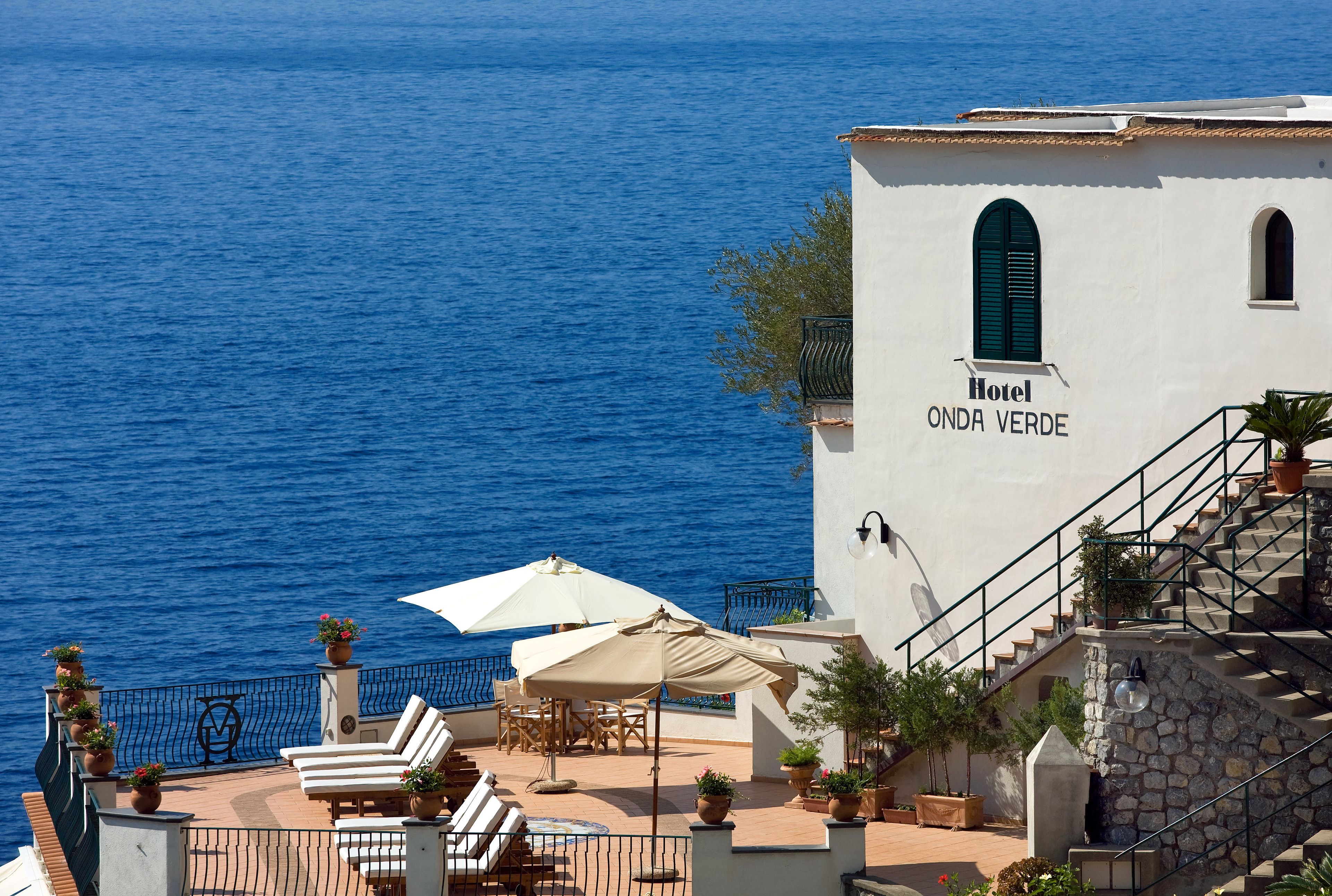 A seaside hotel named 'Hotel ONDA VERDE' with outdoor seating, umbrellas, and a view of the sea.