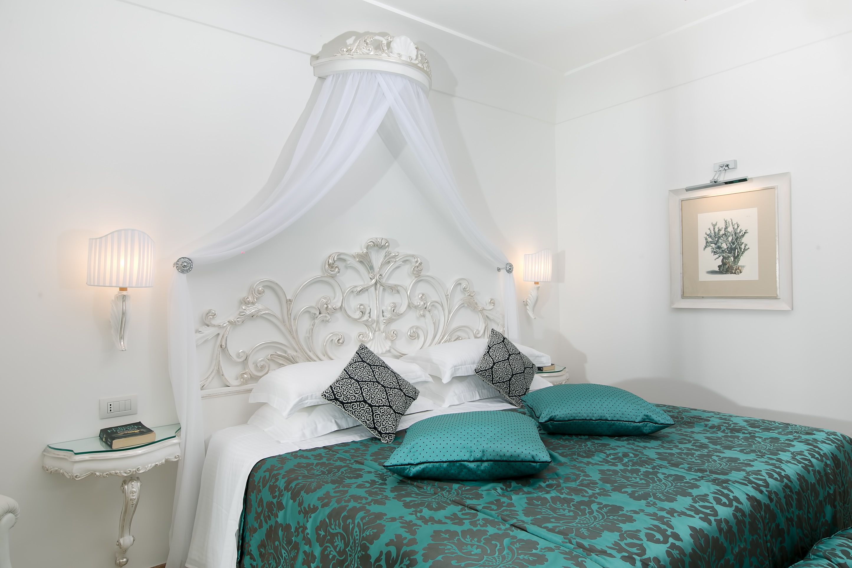 Une chambre à coucher bien rangée, avec un lit à baldaquin, une table de chevet dotée d’une lampe et un tableau encadré accroché au mur.