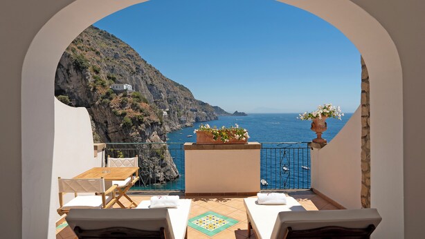 Een balkon met uitzicht op zee, een tafel, stoelen en een bloempot.