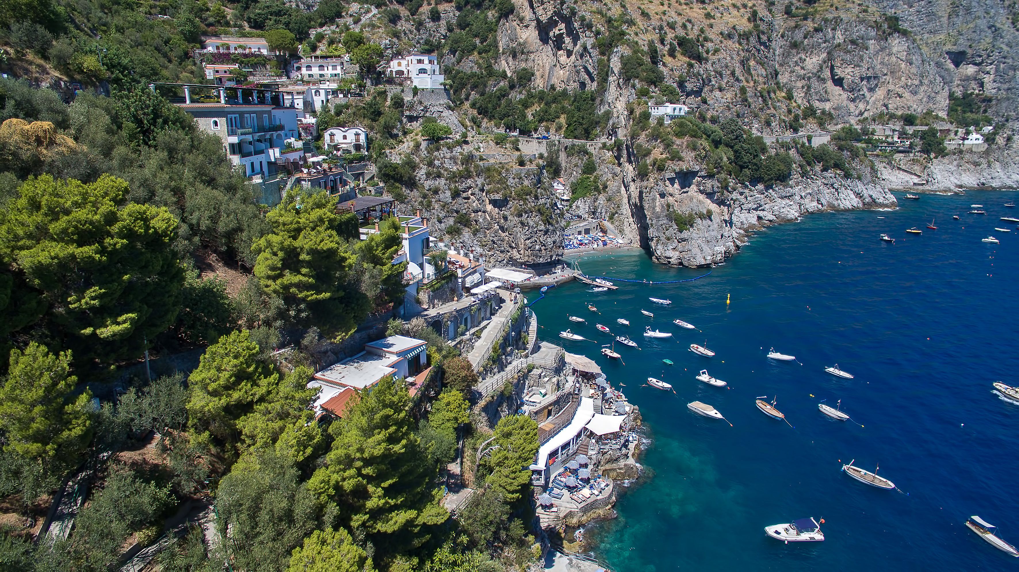 Un pueblo costero con edificios a lo largo del acantilado, una marina con barcos y una costa rocosa.