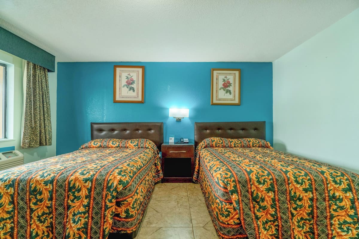 A room with two beds, a nightstand, a lamp, and framed pictures on the wall.