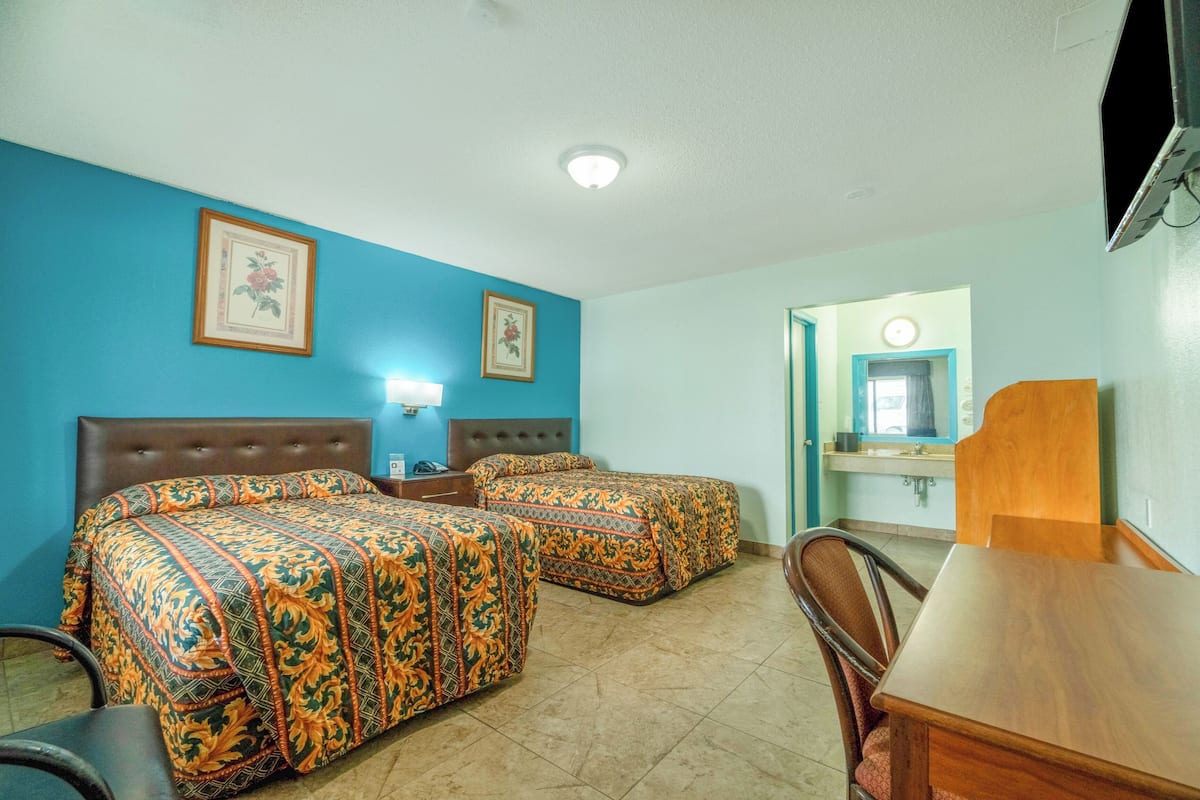 A hotel room with two beds, a wooden headboard, a desk, and a bathroom visible through an open door.
