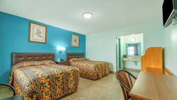 A hotel room with two beds, a wooden headboard, a desk, and a bathroom visible through an open door.