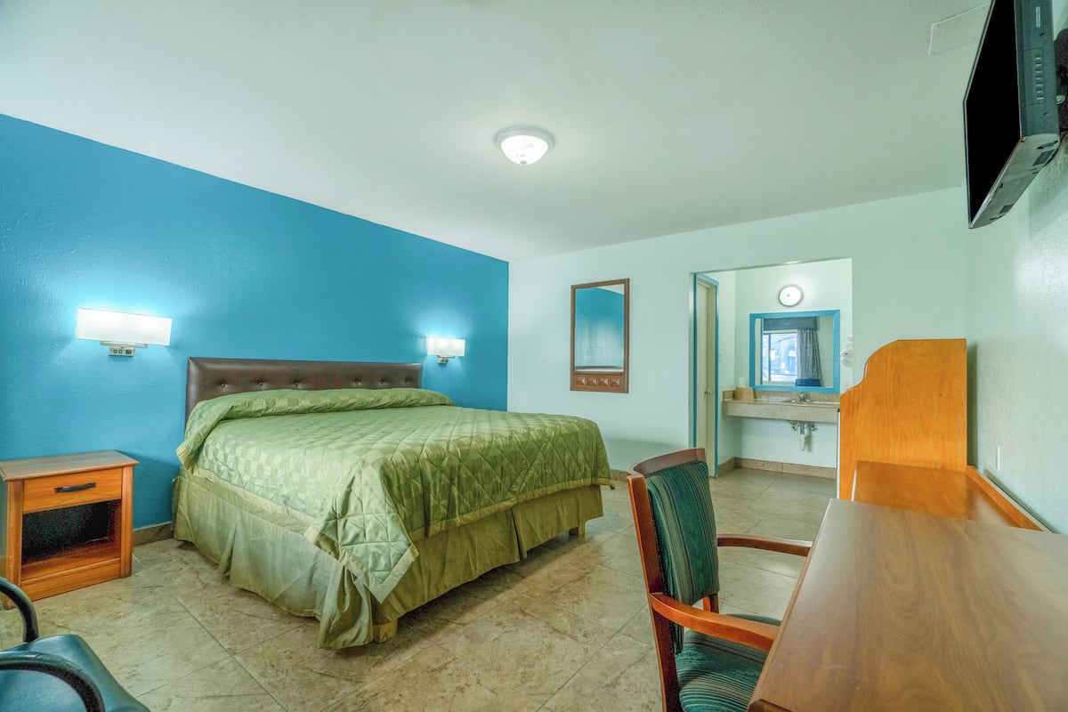 A hotel room with a bed, a desk, a chair, a nightstand, a mirror, and a television.
