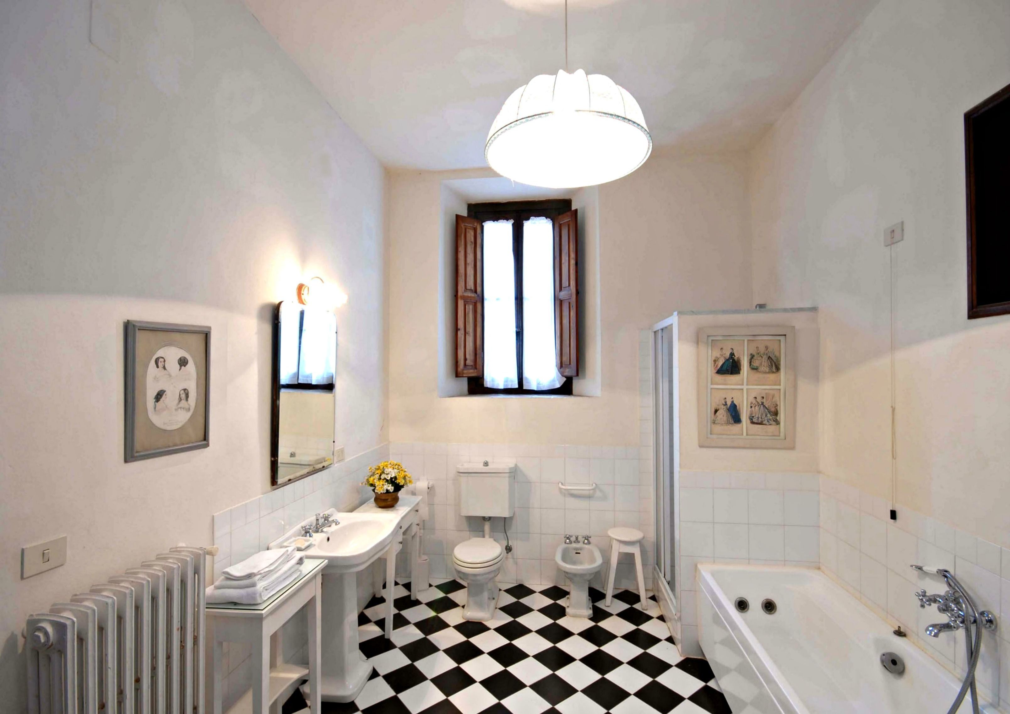 A bathroom with a black and white checkered floor, a white bathtub, a toilet, a bidet, a sink, a mirror, and a framed picture on the wall.