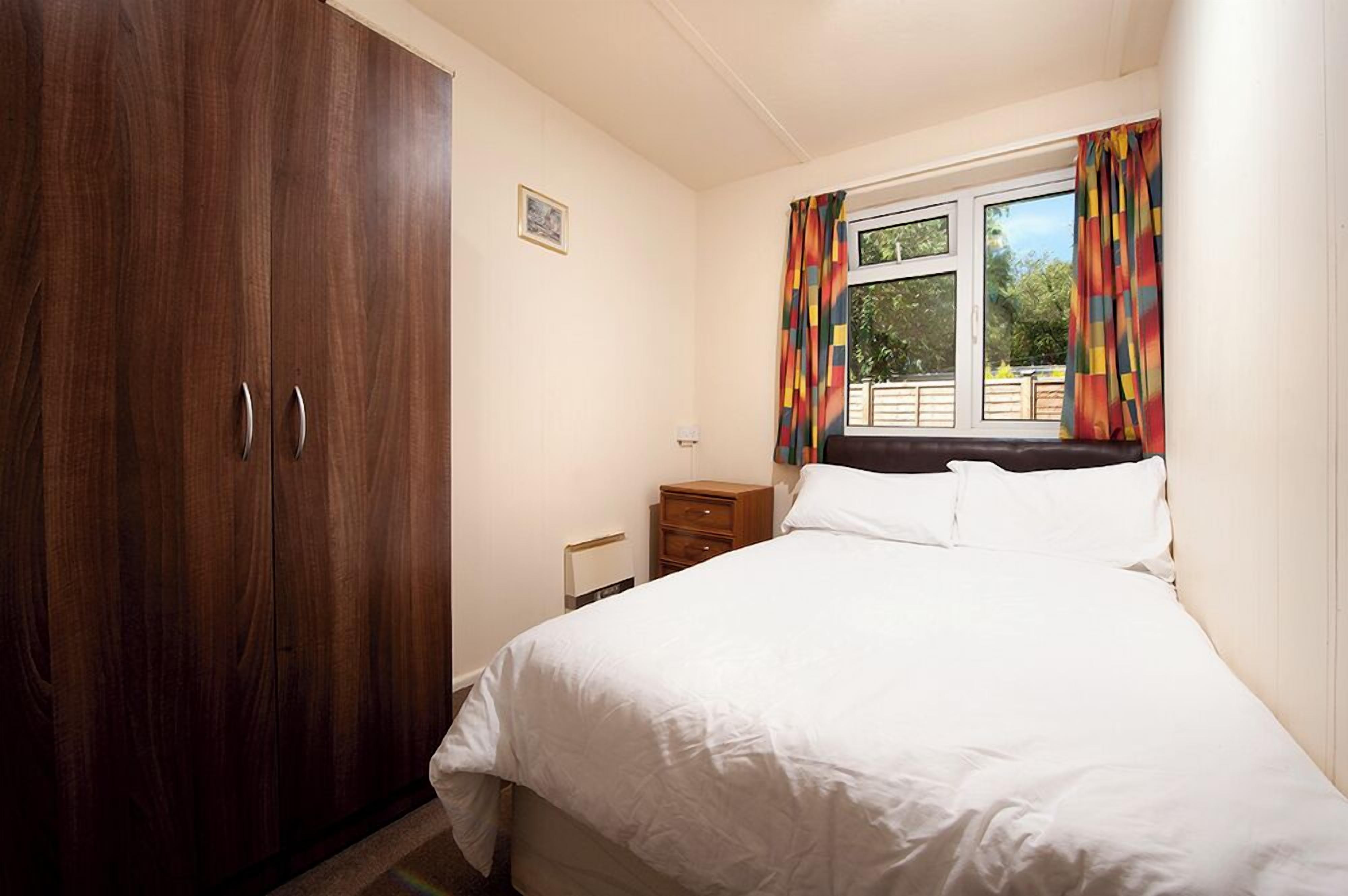 Un dormitorio con un armario amplio, una cama individual, una mesita de noche y una ventana con cortinas.