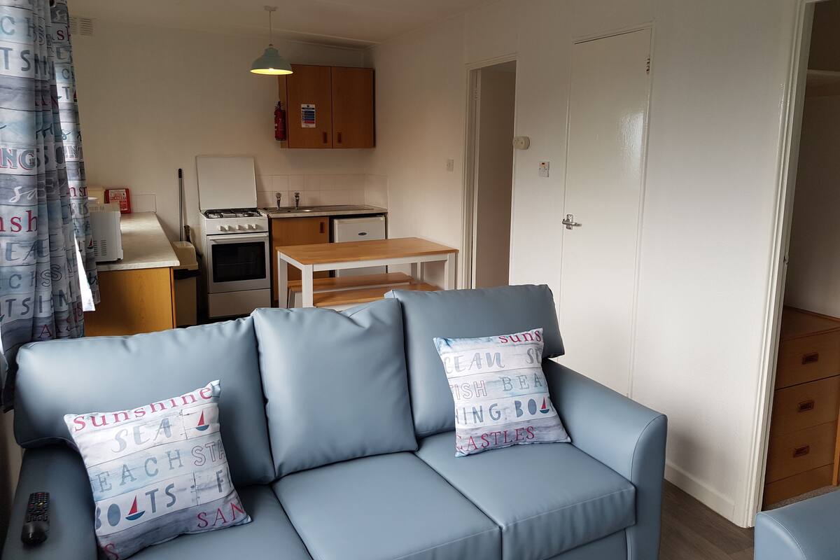 A compact living space with a sofa, a small table, a kitchenette, and a door leading to another room.