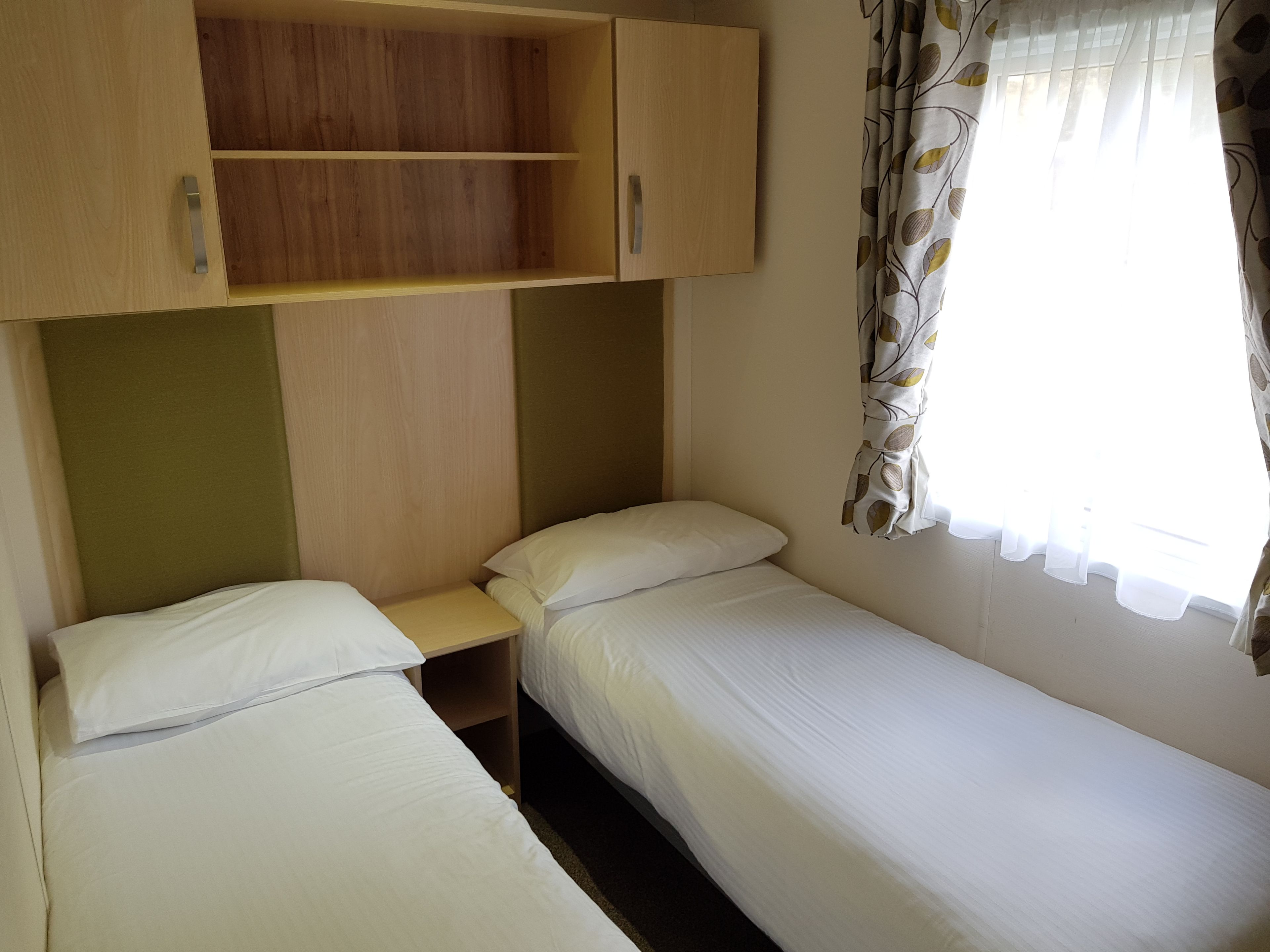 Quarto individual com duas camas, guarda-roupa de madeira e janela com cortinas.