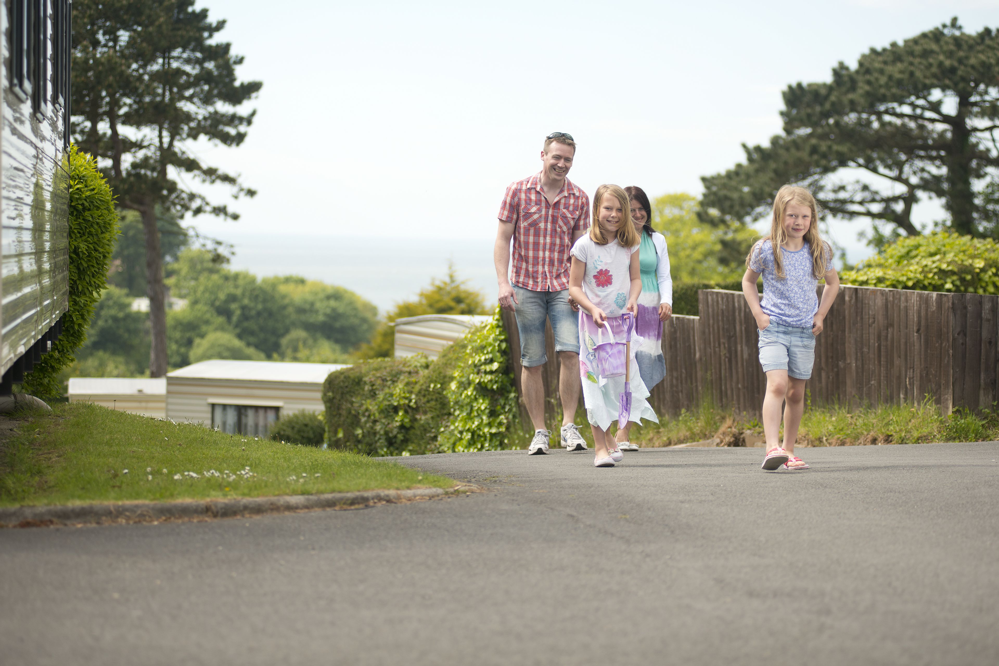 A family walking on a residential street with a house and greenery in the background.