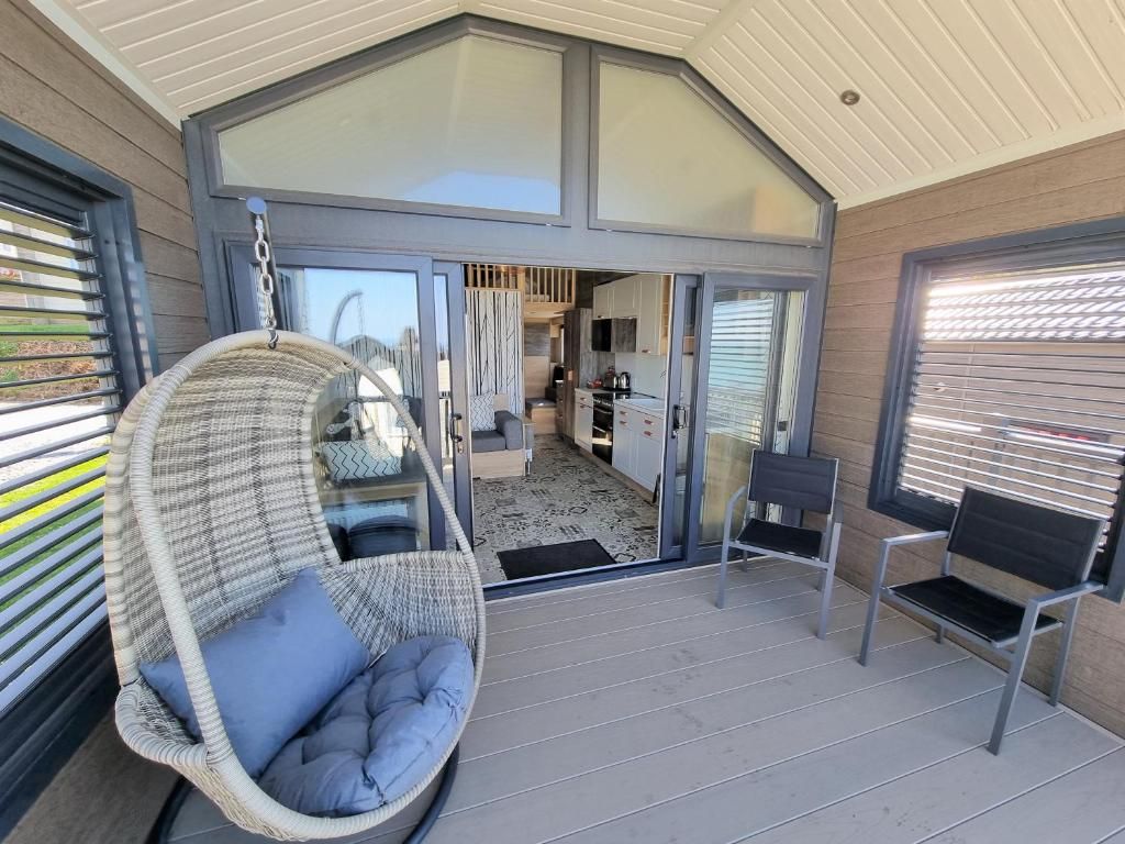 A covered outdoor area with a wicker swing chair, two metal chairs, and a view into a modern kitchen and living space.