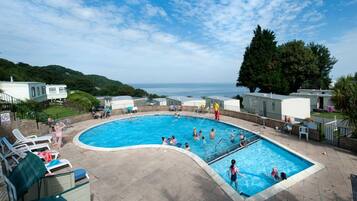 A swimming pool with multiple lanes, surrounded by lounge chairs and a view of the sea.