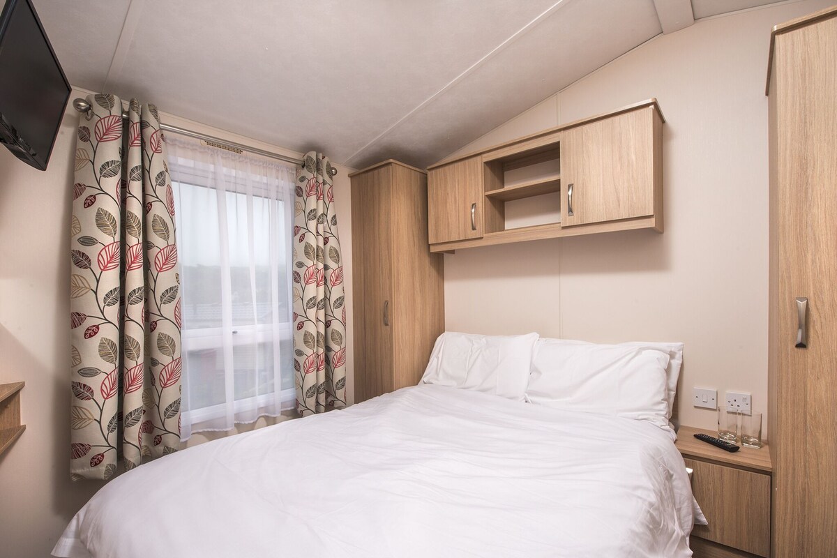 A hotel room with a bed, wooden wardrobe, and a TV mounted on the wall.