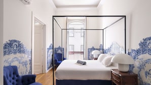 Un dormitorio con cama con dosel, un sillón azul y una mesita de noche con lámpara.