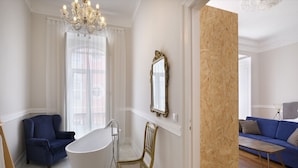 Un baño moderno con una bañera independiente, una silla de madera y un sofá azul en la zona de estar contigua.