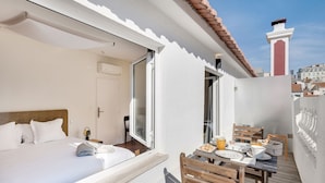 Habitación de hotel con cama, una mesa con alimentos para el desayuno y un balcón con vista a la ciudad.