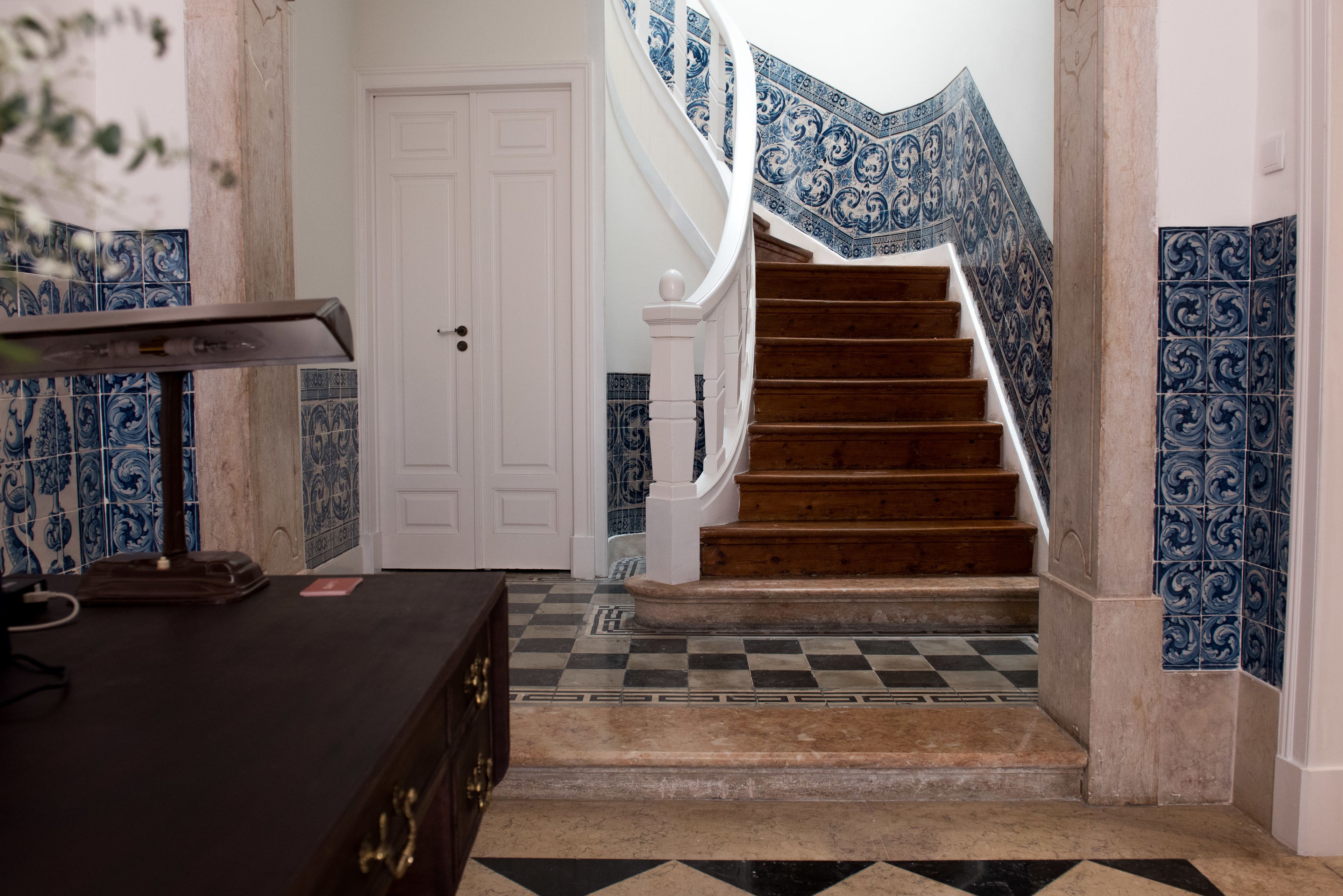 A staircase with blue patterned tiles, a wooden handrail, and a checkered floor.