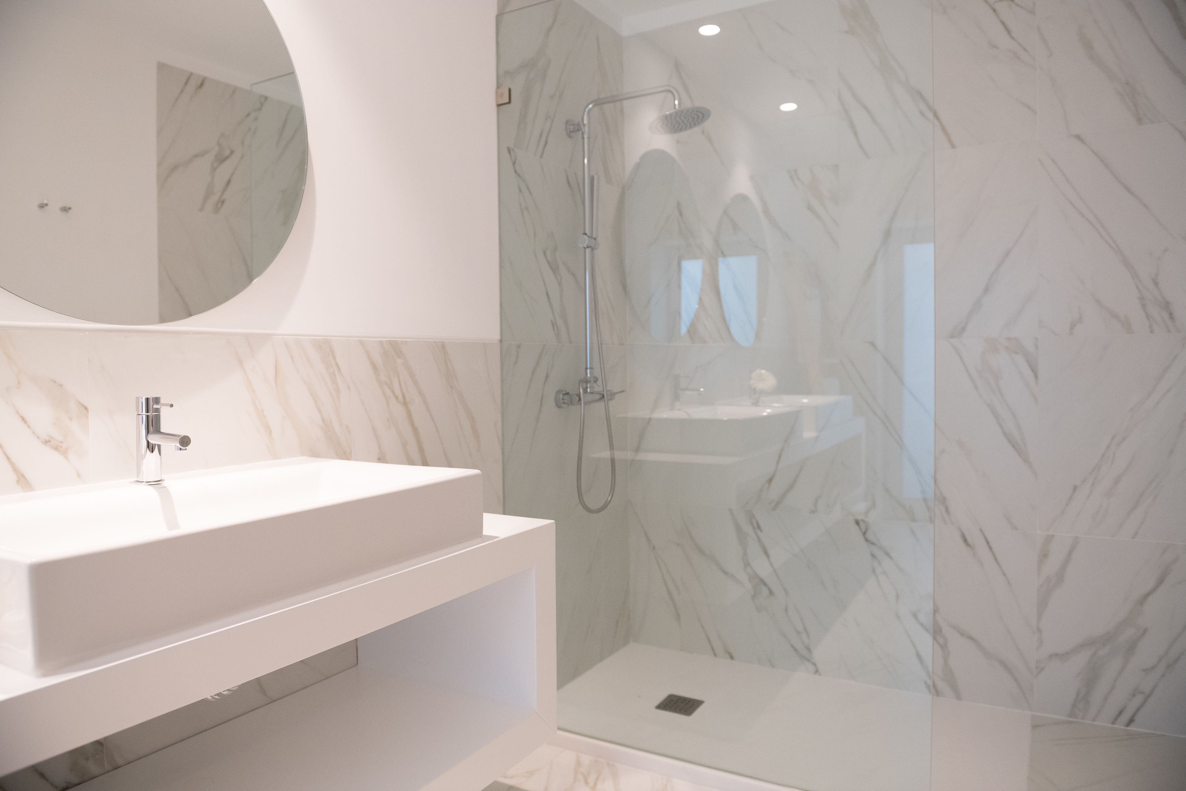 Un baño con lavamanos blanco, un espejo y una zona de ducha con puerta de cristal.