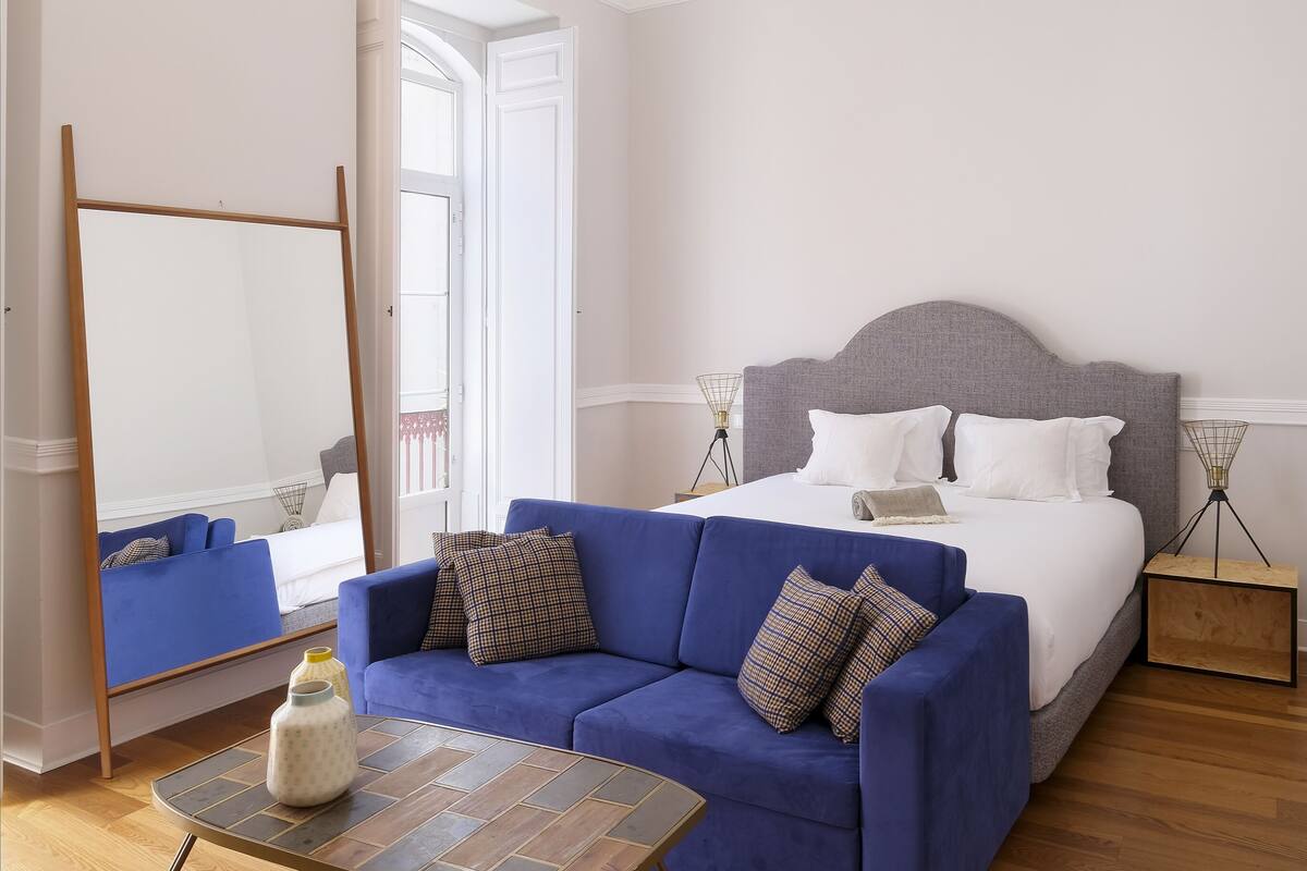 Une chambre à coucher avec un lit, un canapé bleu, une petite table et un miroir.