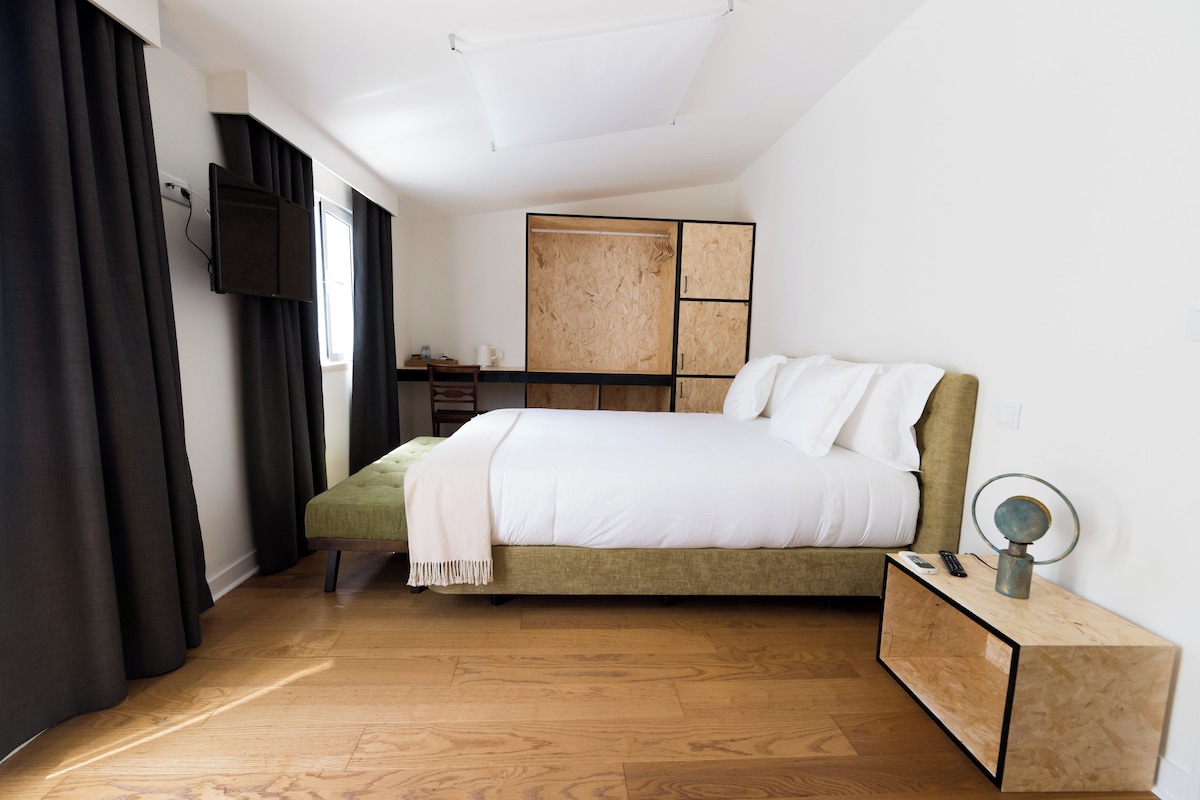 A bedroom with a bed, a bedside table with a lamp, a wardrobe, and a TV mounted on the wall.