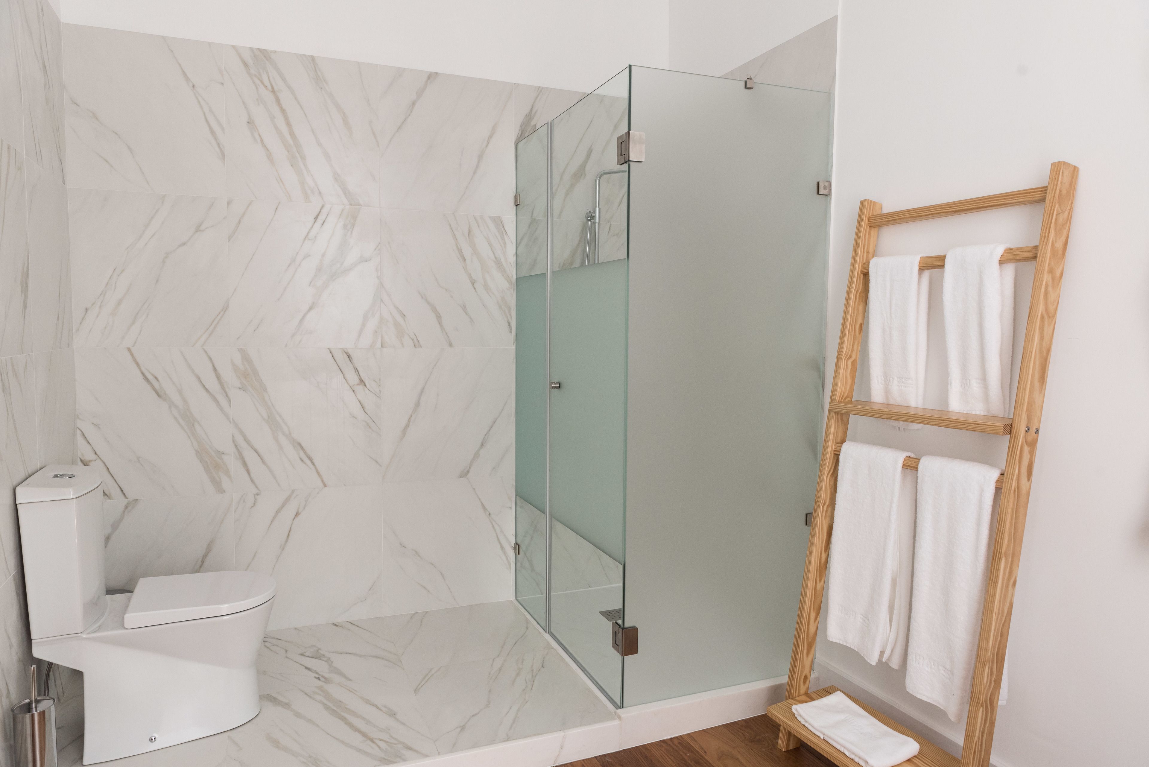 Un baño moderno con cabina de ducha de vidrio, inodoro blanco y toallero de madera.
