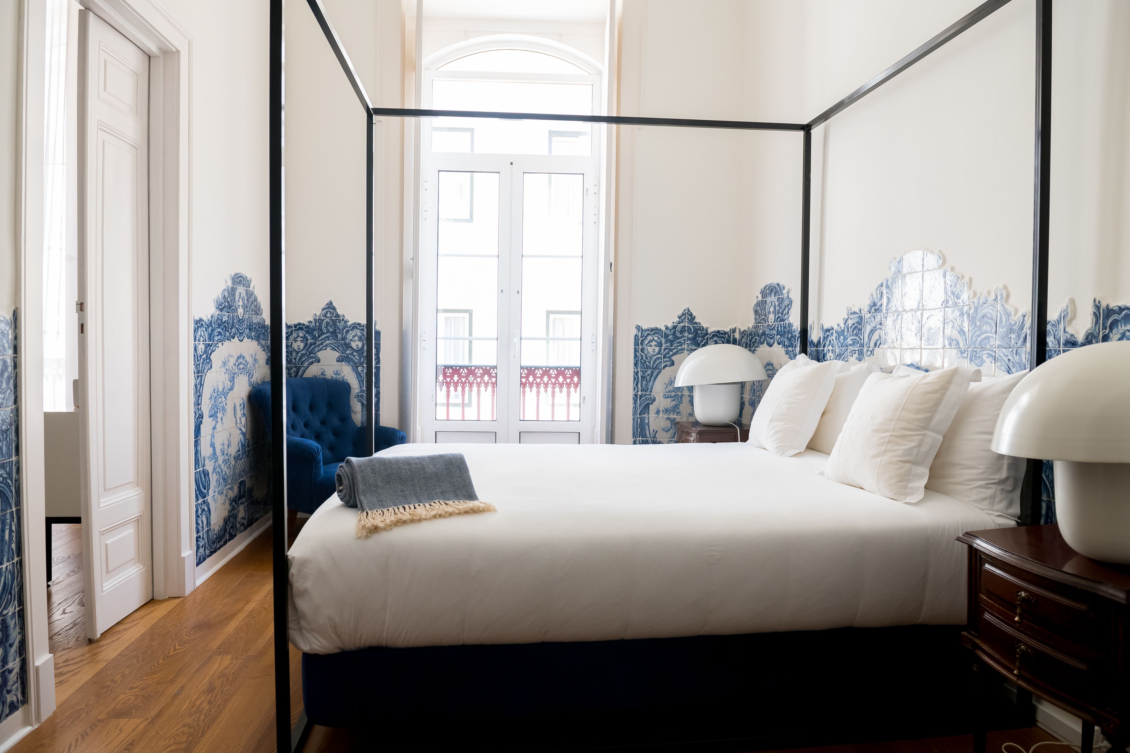 A bedroom with a four-poster bed, a nightstand with a lamp, and blue patterned walls.
