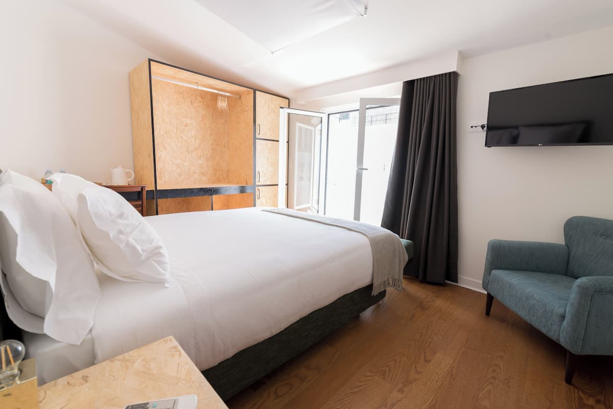 Une chambre d’hôtel avec un lit, une armoire en bois, un téléviseur fixé au mur et un fauteuil bleu.