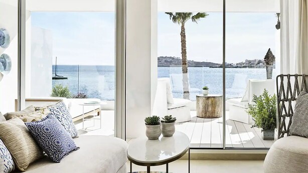 Una sala de estar moderna con un ventanal que ofrece vistas al mar, incluyendo una palmera y un velero.