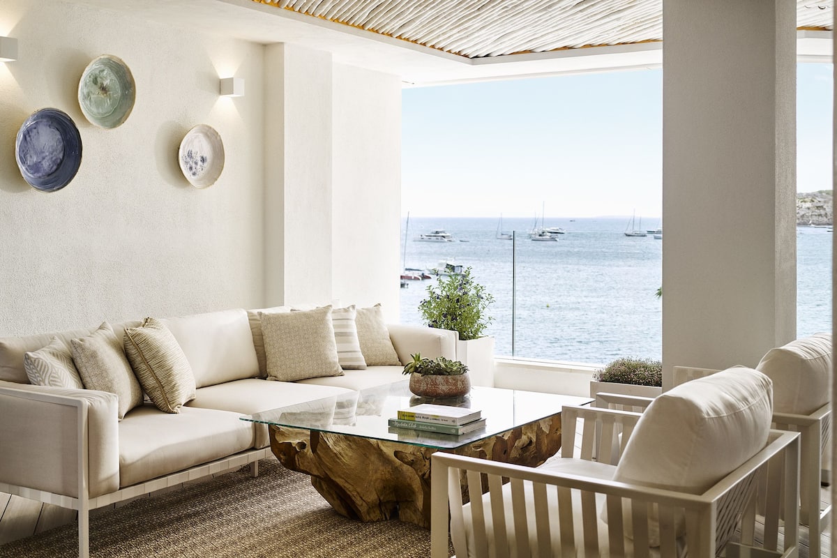 Ett modernt vardagsrum med en vit soffa, ett soffbord i glas och utsikt över havet.