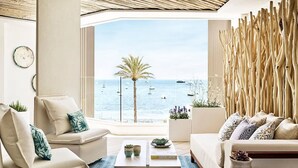 Un moderno salón con vista al mar, que incluye un sofá, una mesa de centro y plantas decorativas.