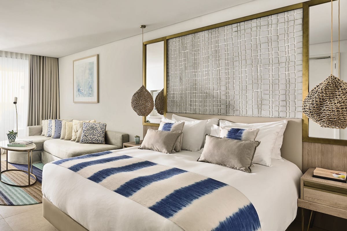 Ett modernt hotellrum med en stor säng, en soffa, ett litet sidobord och utsikt över havet.