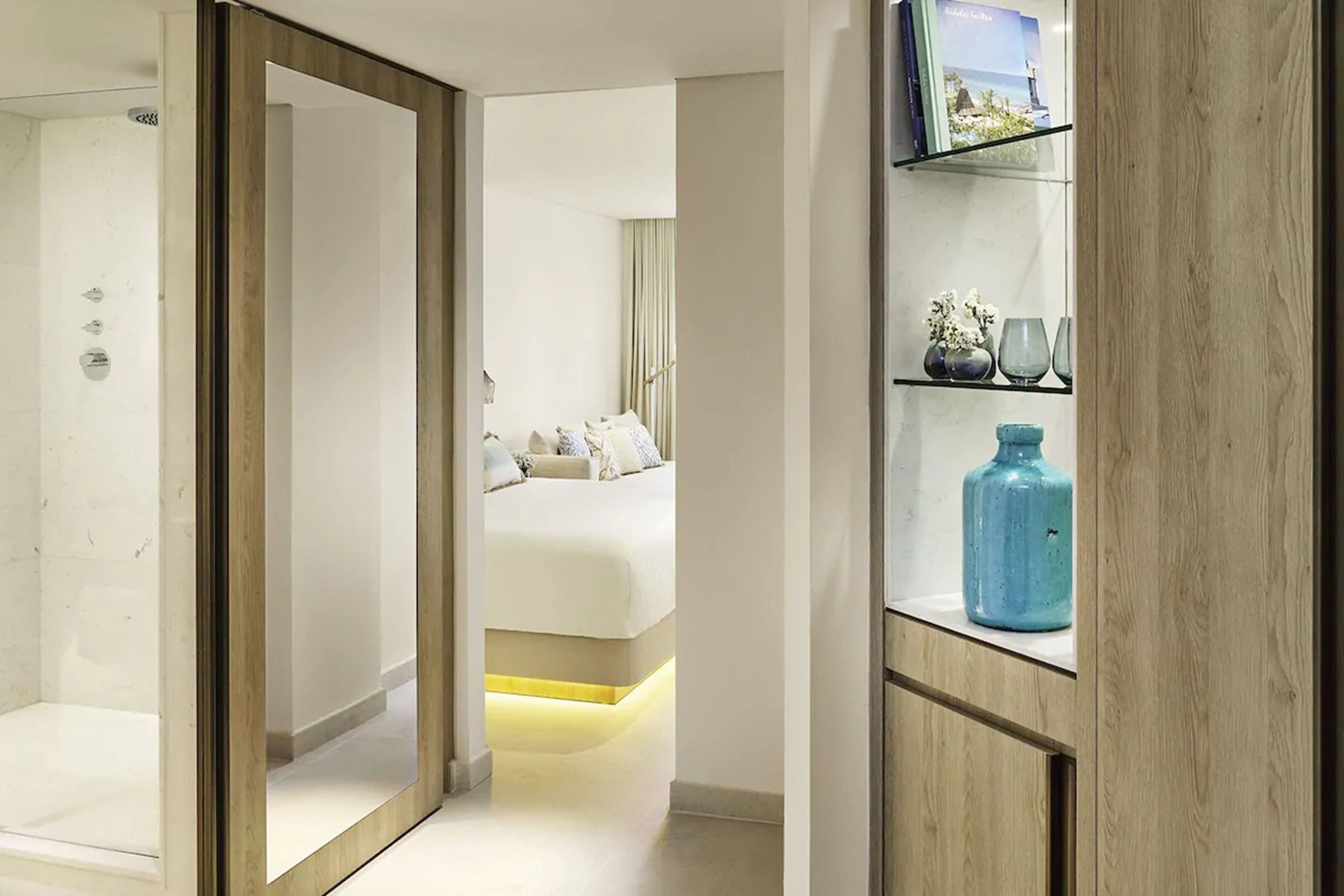 Een hotelkamer met een bed, nachtkastje, plank met decoratieve items en een spiegel.
