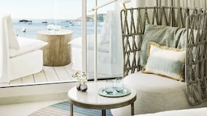 Una sala de estar moderna con vistas al mar, que incluye un sofá, una mesa redonda de madera con dos vasos y una silla blanca.