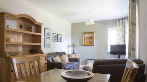 A dining area with a wooden table, chairs, a wooden cabinet, a sofa, a television, and a lamp. - LETS Quiet Cul-de-Sac Apartment (Cambridge)