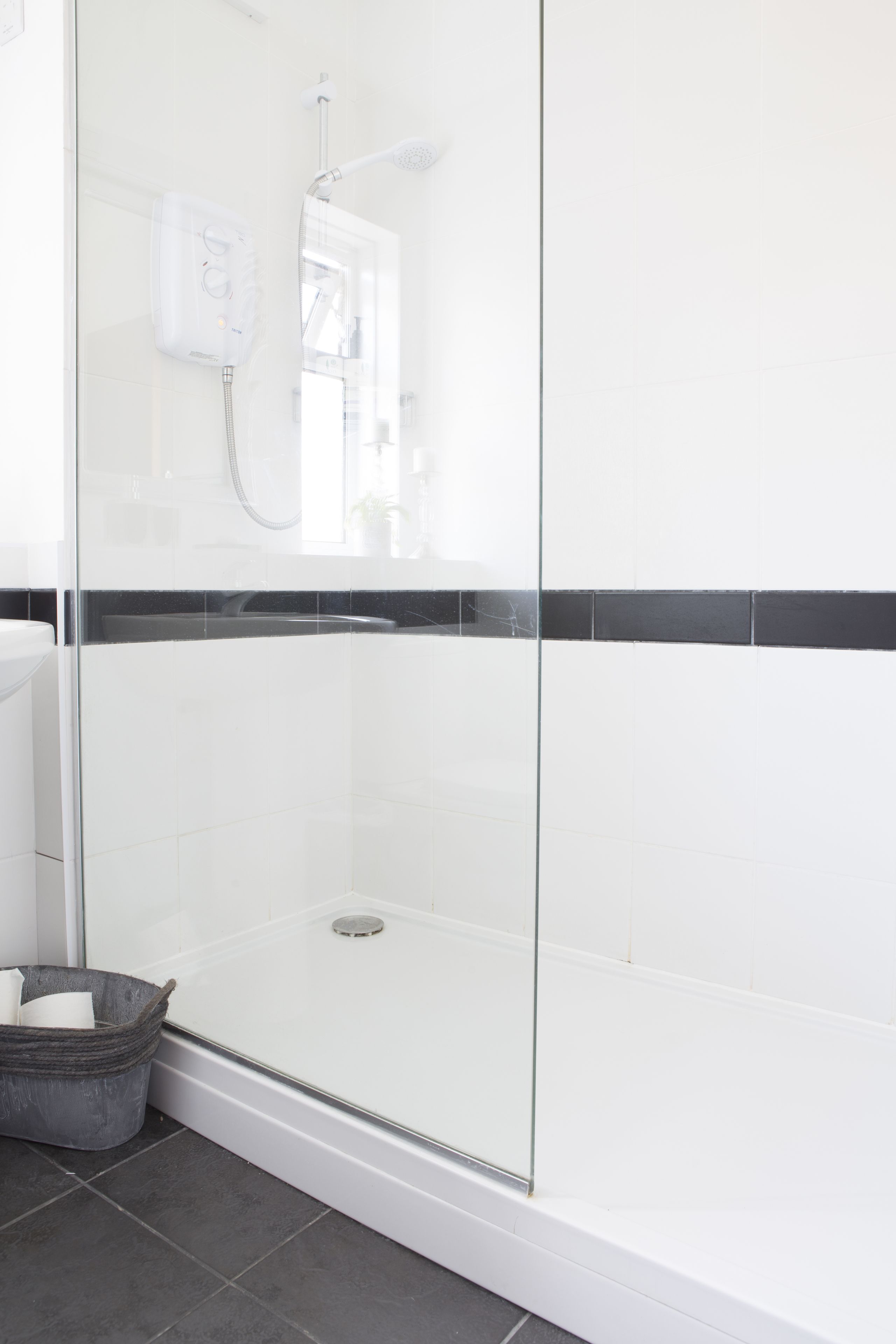 A modern bathroom with a glass-enclosed shower, white tiles, and a black horizontal accent strip.