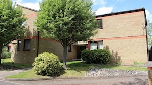 A two-story brick building with a flat roof, a small front porch, and a well-maintained lawn with a tree and bushes. - LETS Quiet Cul-de-Sac Apartment (Cambridge)