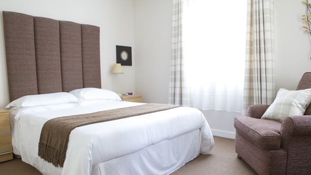 A neatly arranged bedroom with a large bed, a bedside table, a lamp, and a chair. - LETS Quiet Cul-de-Sac Apartment (Cambridge)