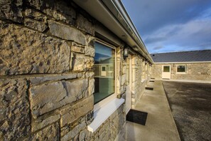 A stone building with a window and a door, a concrete pathway, and a paved area. - The Red Cottage & Stables (Sligo)