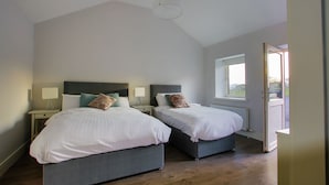 A bedroom with two beds, a window, and a door leading outside. - The Red Cottage & Stables (Sligo)