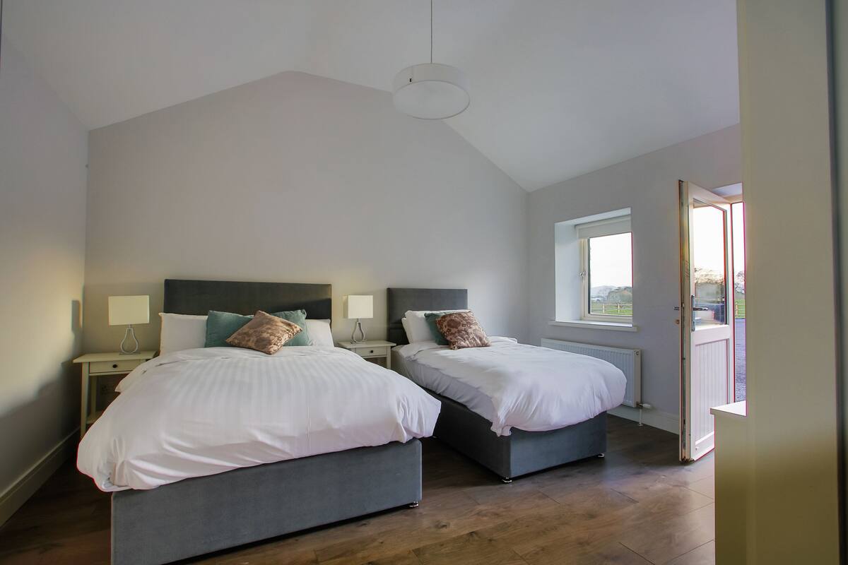 A bedroom with two beds, a window, and a door leading outside.