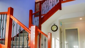 A staircase with wooden railings and metal balusters, carpeted steps, and a clock on the wall. - The Red Cottage & Stables (Sligo)