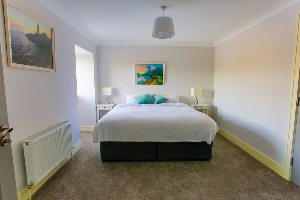 A bedroom with a bed, a nightstand, a lamp, a painting, and a radiator.