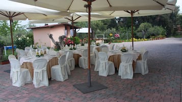 Een buitenterras met ronde tafels klaar voor dineren, omringd door parasols en stoelen.