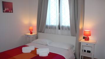 Hotelkamer met een bed, twee nachtkastjes met lampen, een raam met gordijnen en een aan de muur hangend schilderij.