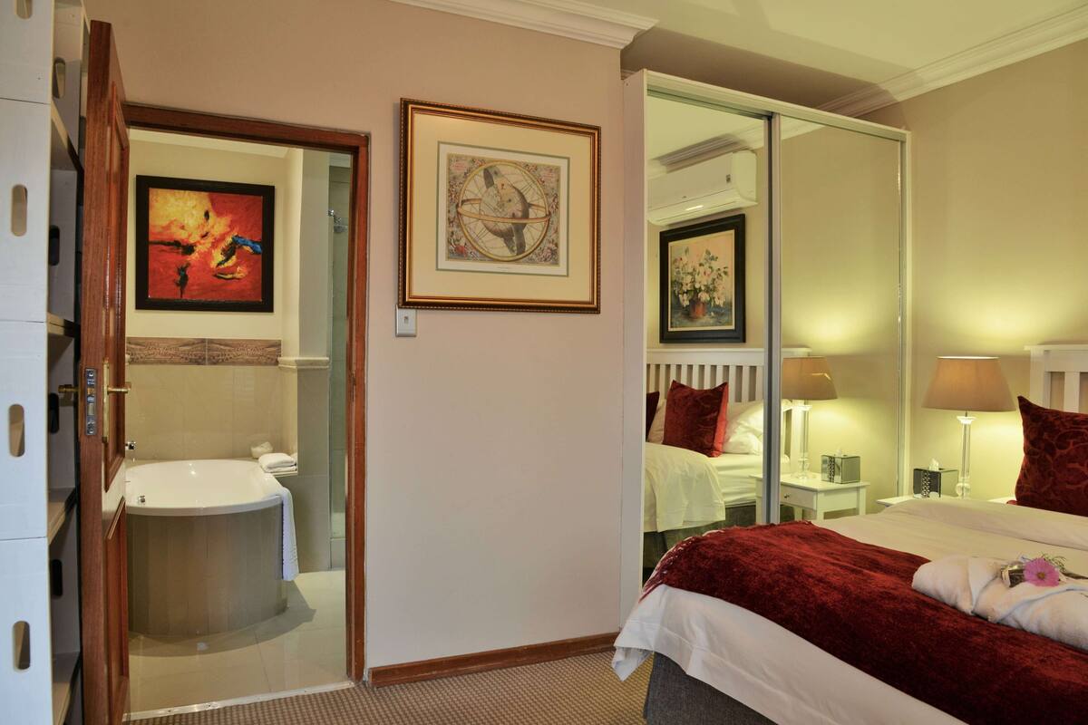 Una habitación de hotel con una cama grande, un baño con bañera y un espejo que refleja la habitación.