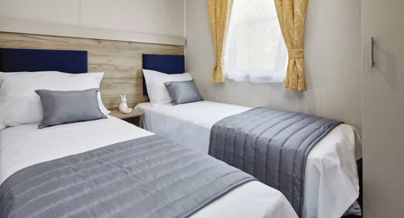 A hotel room with two beds, a nightstand, and a window with curtains.