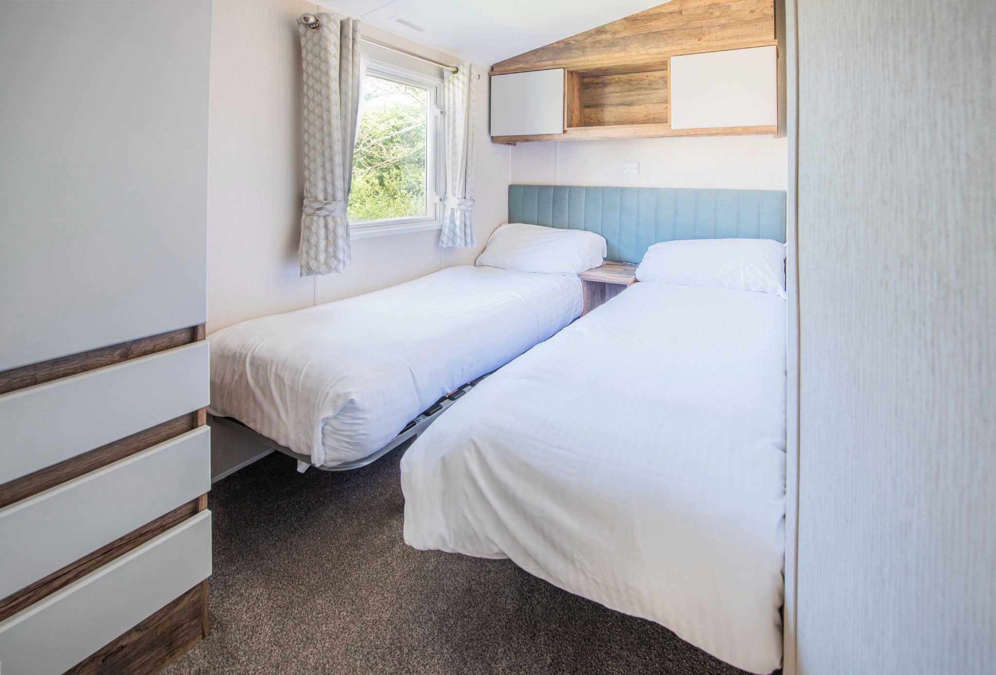 A small, clean room with two single beds, a window with curtains, and a wooden headboard.