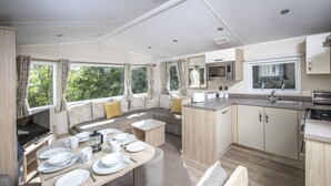 A modern RV kitchen with a dining area, a microwave, a sink, and a large window offering a view of greenery. - South Bay Holiday Park (Brixham)