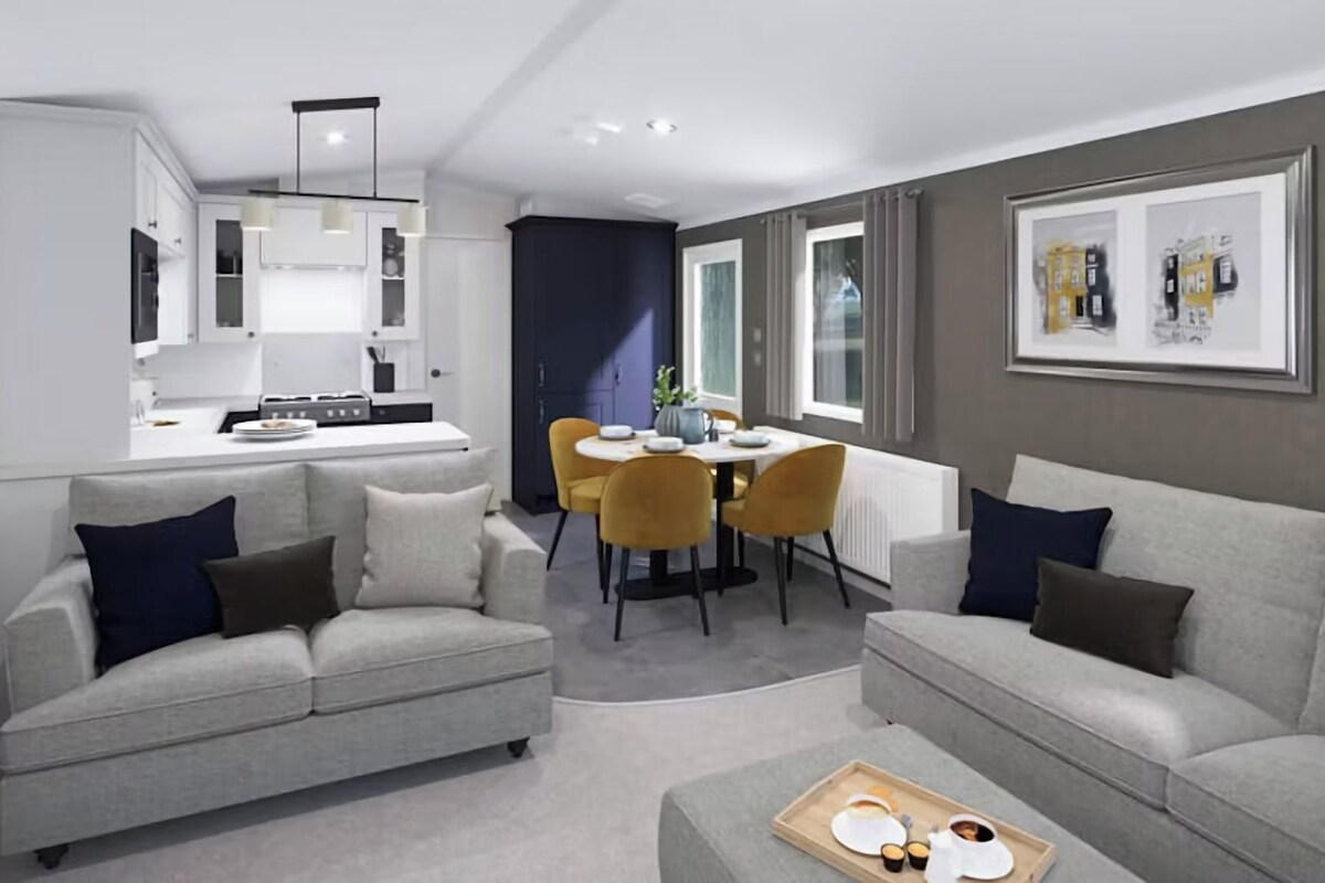 A modern living room with grey sofas, a dining area with yellow chairs, and a kitchen in the background.