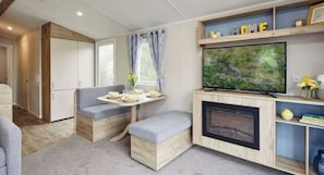 A compact living space with a sofa, a small table with a vase, a television, and a fireplace. - South Bay Holiday Park (Brixham)