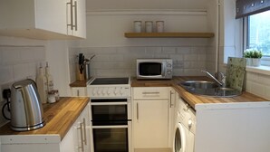 Kompakti keittiö, jossa on valkoiset kaapit, mikroaaltouuni, vedenkeitin, liesi ja pesukone.